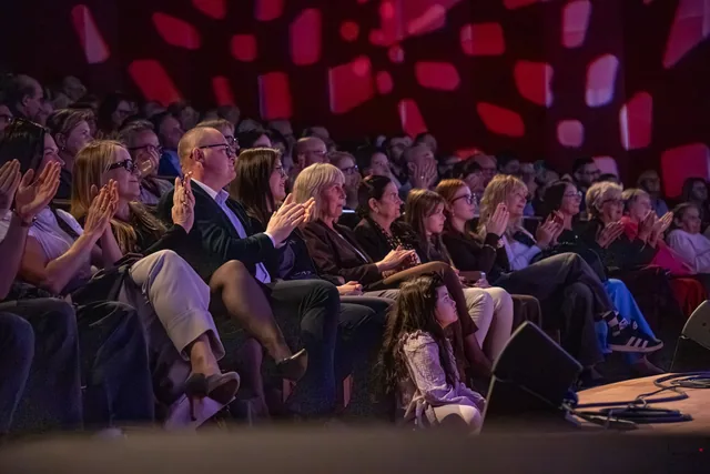 Publiczność siedząca w rzędach na widowni.